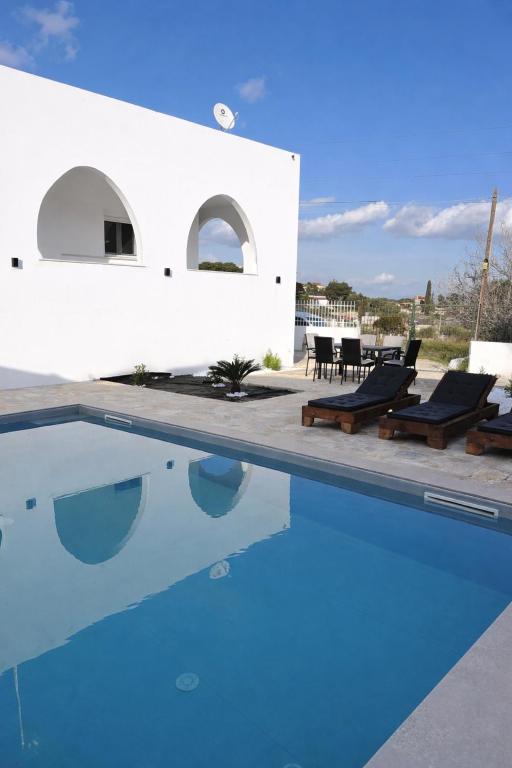 a swimming pool with two chairs and a house at Villa Pano Salamina in Ambelákia