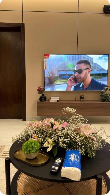 a room with a table with flowers and a tv at Spacious Two-Bedroom Apartment with a Large Living Room, comfortable and well organized, perfect for a relaxing stay in Jeddah