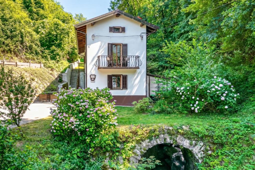 a small white house with a balcony in a garden at House By The Stream in Soča Valley - Happy Rentals in Avče