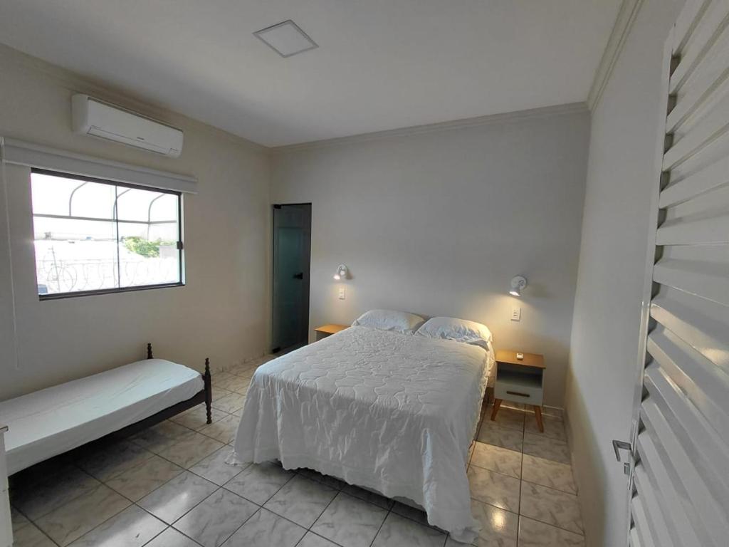a white bedroom with a bed and a window at Nosso Lar casa inteira, completa e independente in Barra do Garças