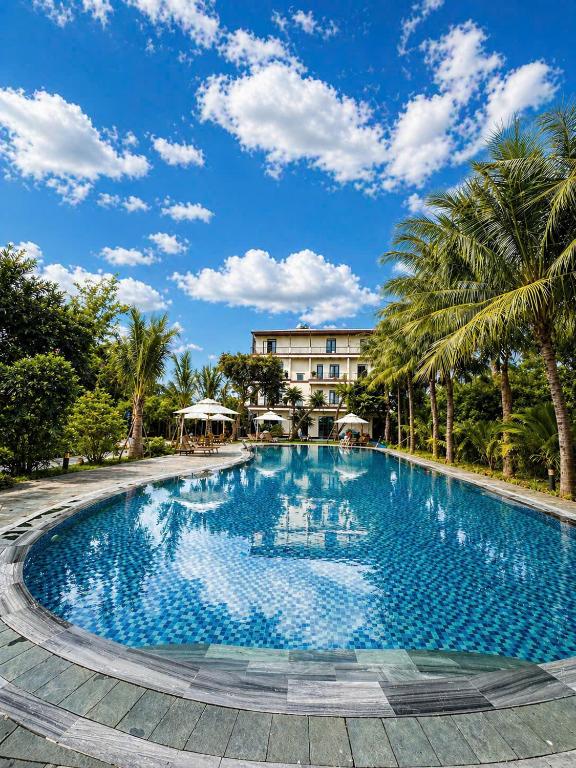 a large swimming pool with palm trees in front of a building at An Velora Boutique Hotel in Lai Nghê (2)
