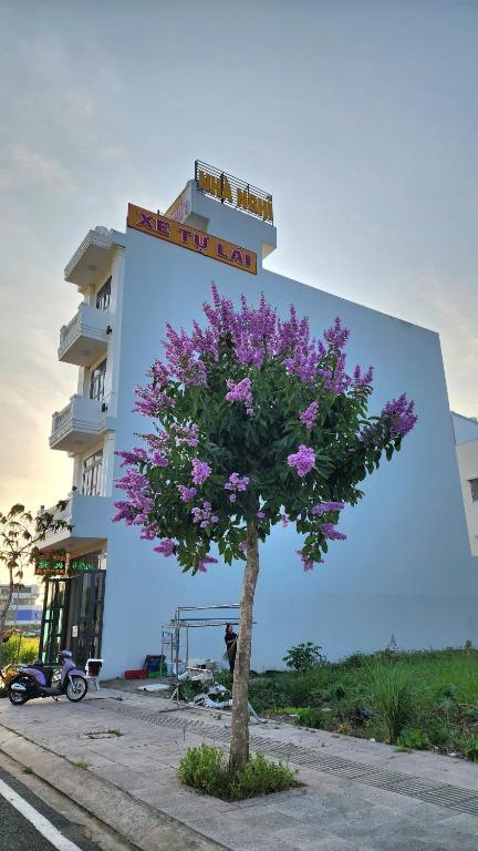 a tree with purple flowers in front of a building at Nhà nghỉ Thanh Thư 2 in Vị Thanh