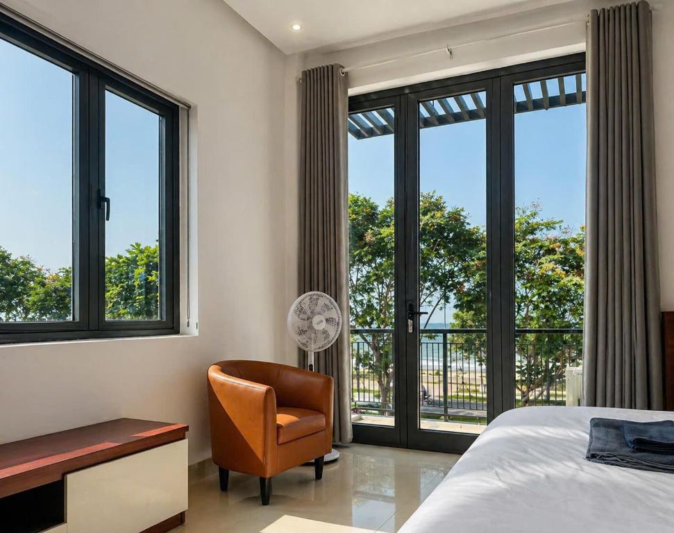 a bedroom with a bed and a chair and windows at NOAM Stay - Sea Corner in Danang