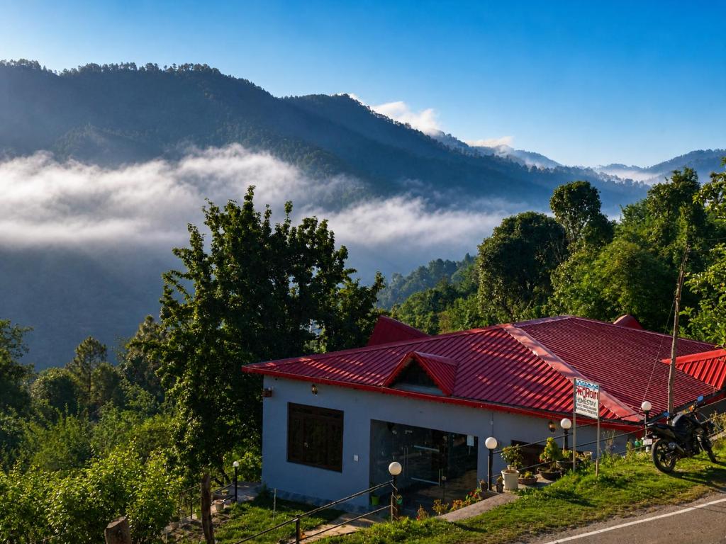 a house with a red roof with mountains in the background at A Home Above the Clouds Riturain Mukteshwar in Mukteshwar