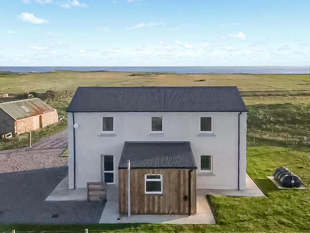 a white house with a black roof in a field at Husabost House in Carinish