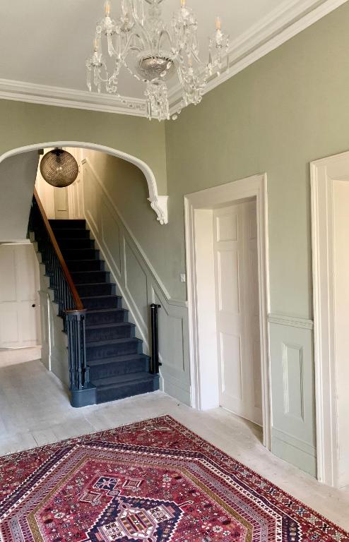 a room with a staircase with a chandelier and a rug at Norwood in Rushbrooke