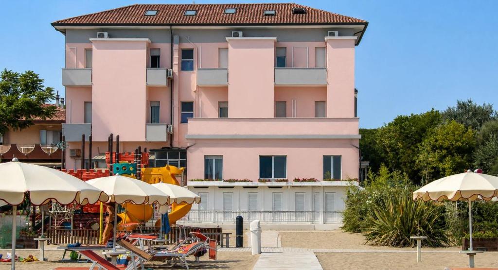 a pink building with tables and umbrellas in front of it at Hotel Maria Luisa in Rimini