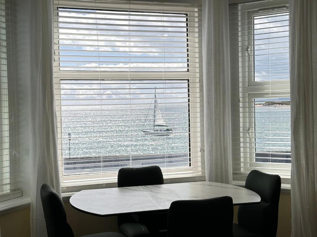 a table and chairs in front of a window with a sailboat in the water at Exmouth Devon Luxurious Flat OverlookingThe Sea in Exmouth