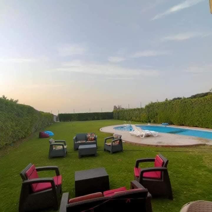 a group of chairs sitting in the grass next to a pool at فيلا غرناطه الساحل الشمالي in Dawwār al Ḩajj Aḩmad
