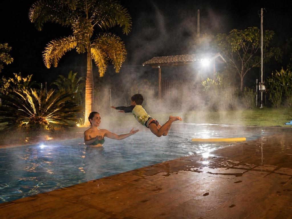 two boys jumping into a swimming pool at night at Casa Firenze - Piscina aquecida até no frio! in Rio Manso