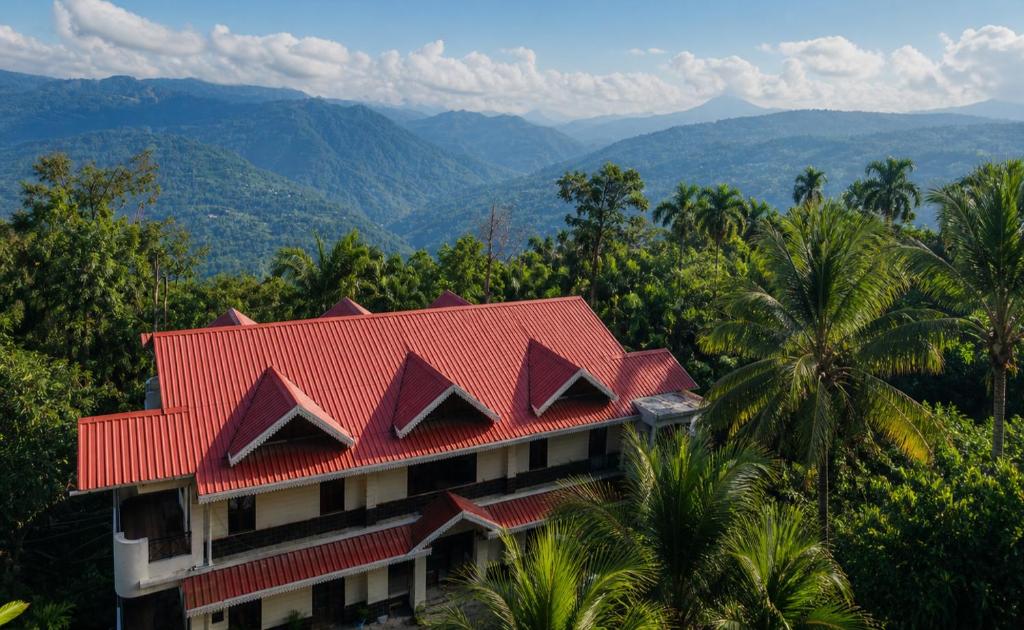 a building with a red roof with mountains in the background at Kalimpong Bungalow in Kalimpong
