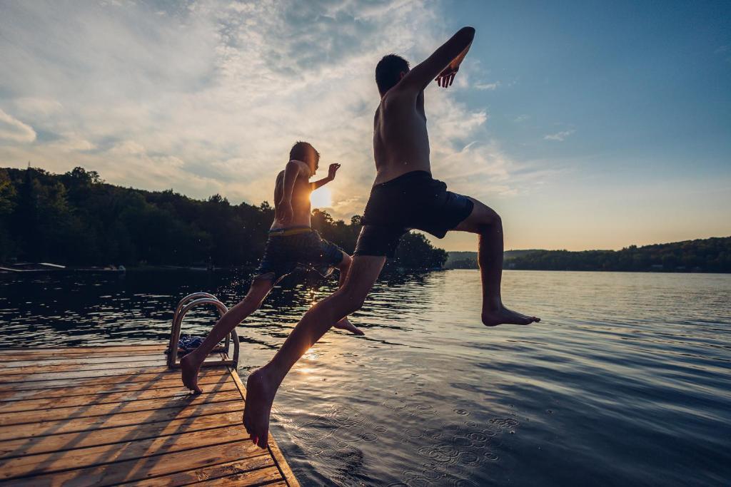 two young men jumping off a dock into the water at Diamond Lakehouse | SUP, Canoe, BBQ, Aurora Magic in Highland Grove