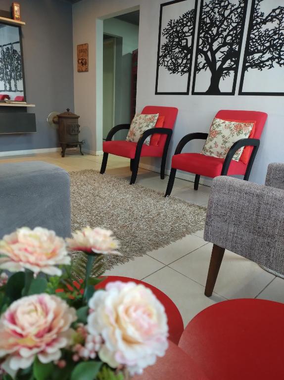 a living room with red and black chairs and flowers at Apartamento London - Centro Nova Petrópolis in Nova Petrópolis