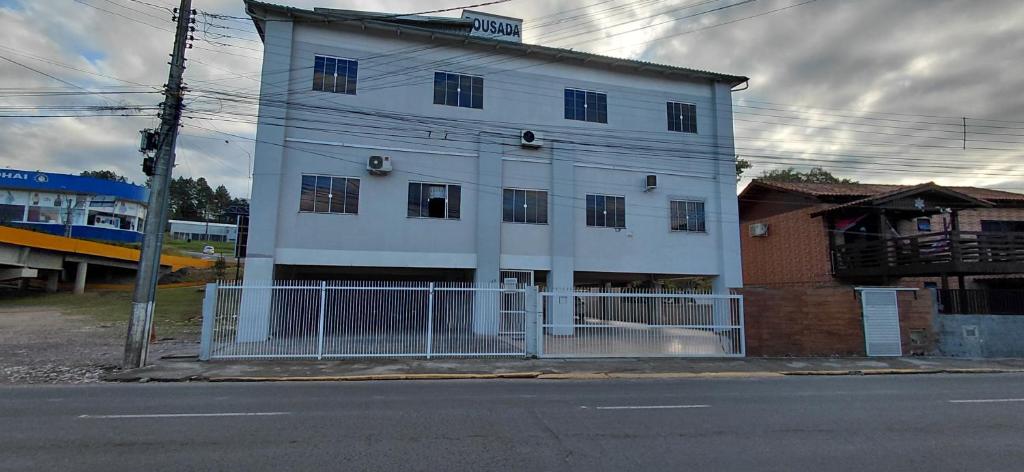 a white building with a fence next to a street at Pousada Familiar 01 in Rio do Sul