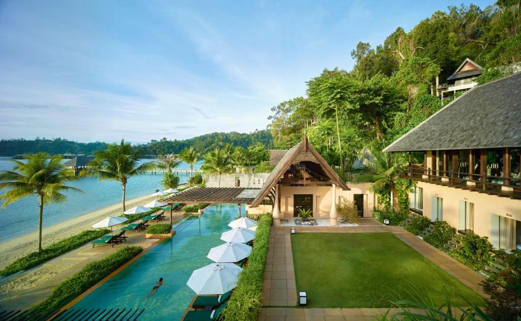 eine Luftansicht eines Resorts mit Pool und Sonnenschirmen in der Unterkunft Gaya Island Resort - Small Luxury Hotels of the World in Gaya Island