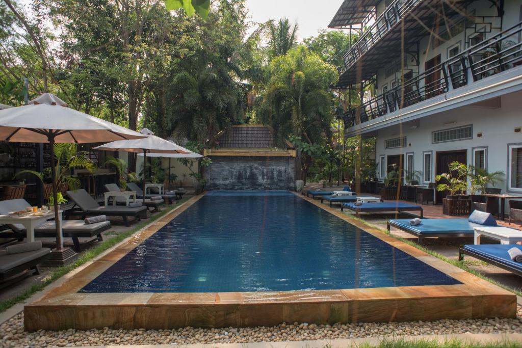 a pool at a hotel with chairs and umbrellas at The Local Time Village in Siem Reap