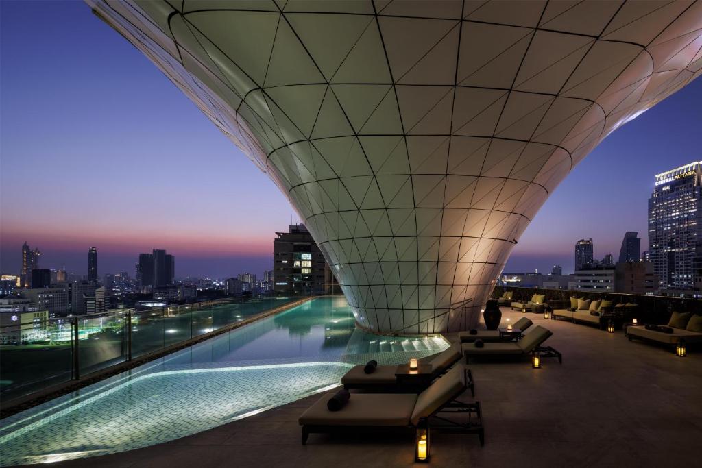 A rooftop pool deck wraps around a dramatic canopy with loungers facing the city at twilight.