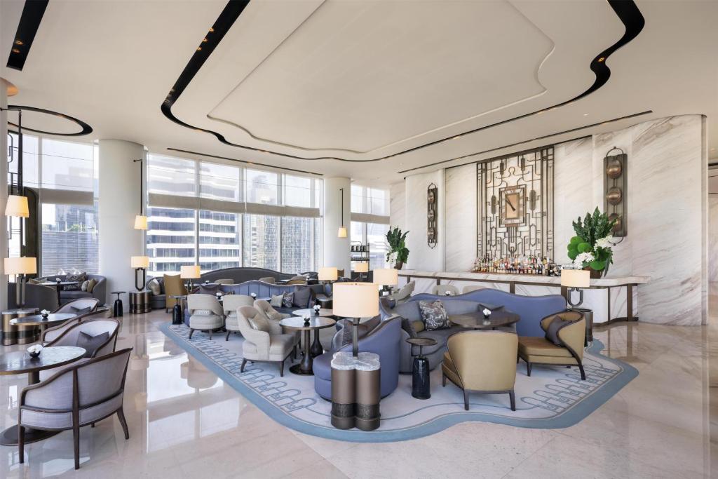 A spacious lobby salon with blue sofas, armchairs, marble walls and large city-facing windows.