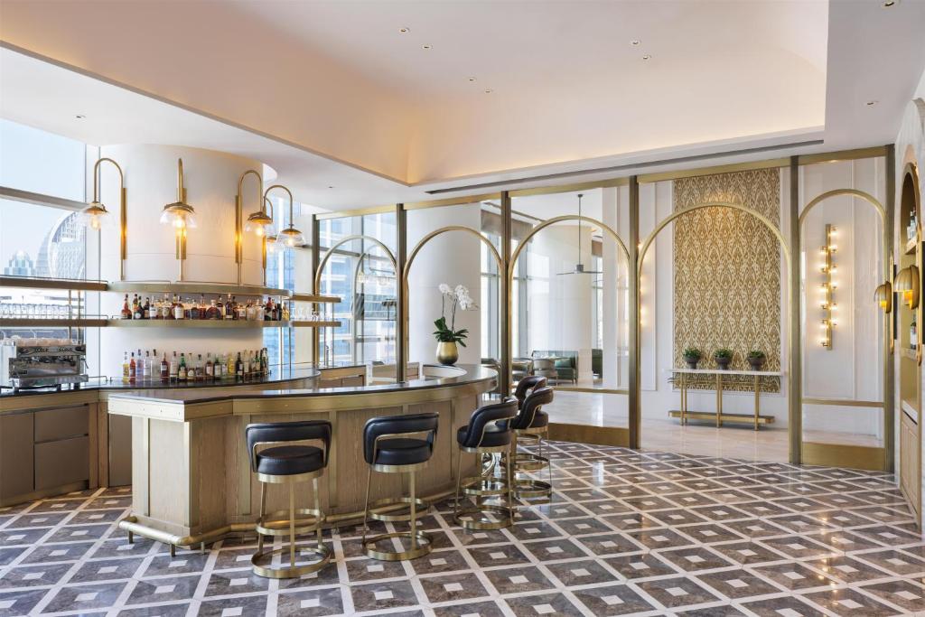 A bright lobby bar with a compact counter, four visible stools, and ornate gold detailing.