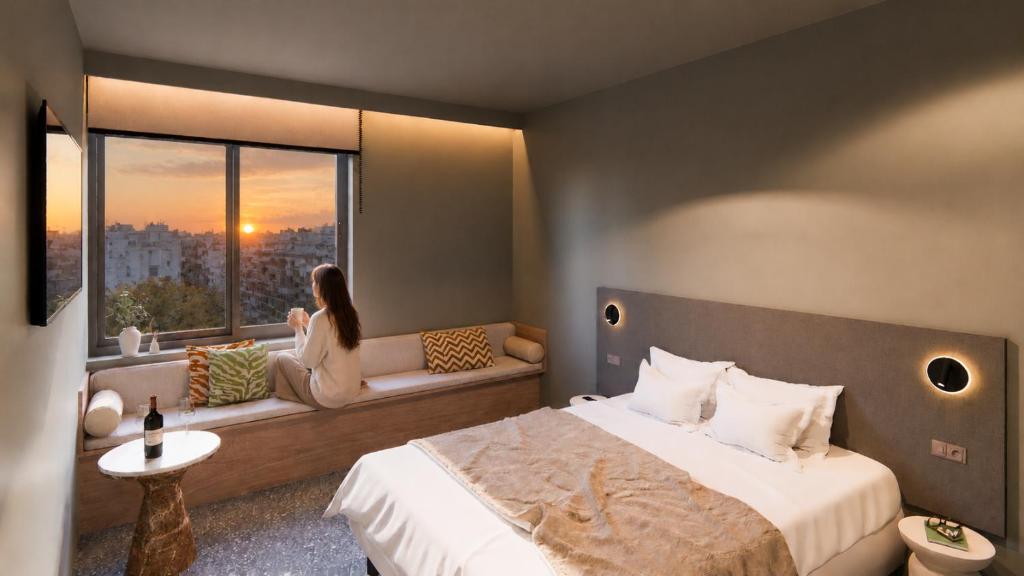 a woman sitting on a couch looking out of a bedroom window at Nixon Downtown, a member of Nixon Hotels in Athens