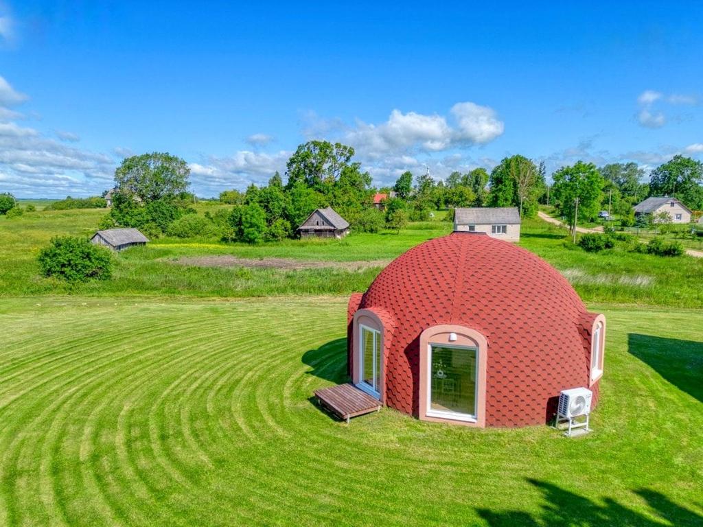 a small red dome house on a green field at Kupolo patyrimas in Jurgeliškė