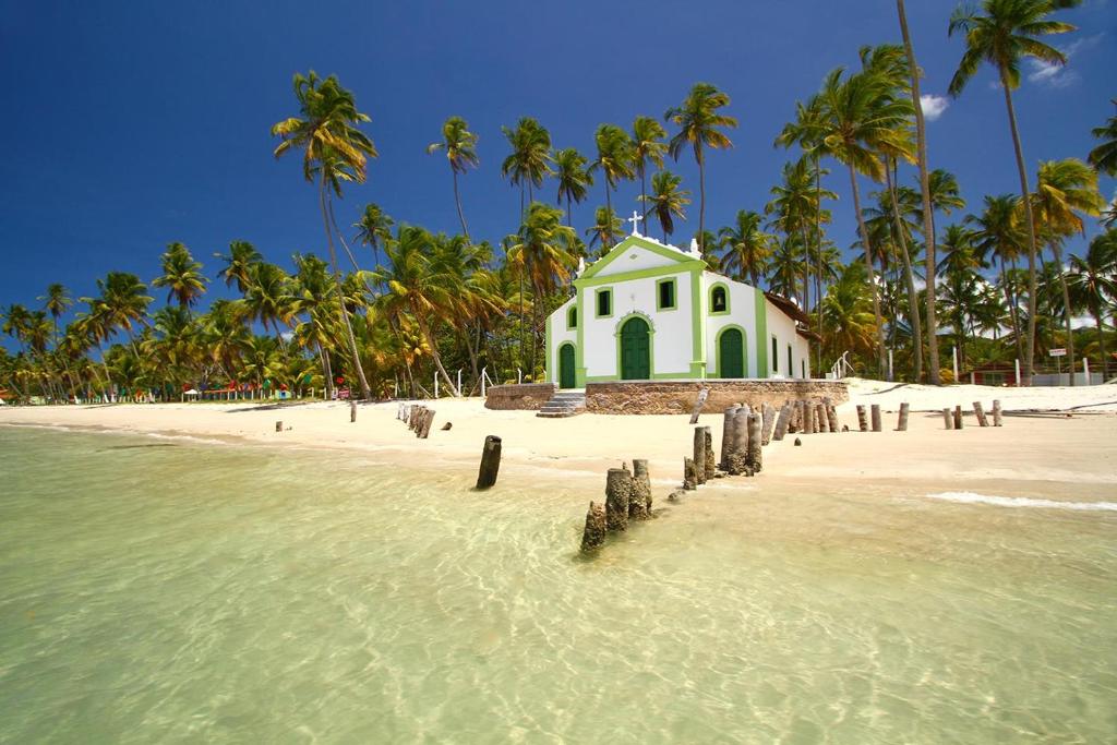 a white building on a beach with palm trees at Flat Carneiros Beach Resort in Tamandaré