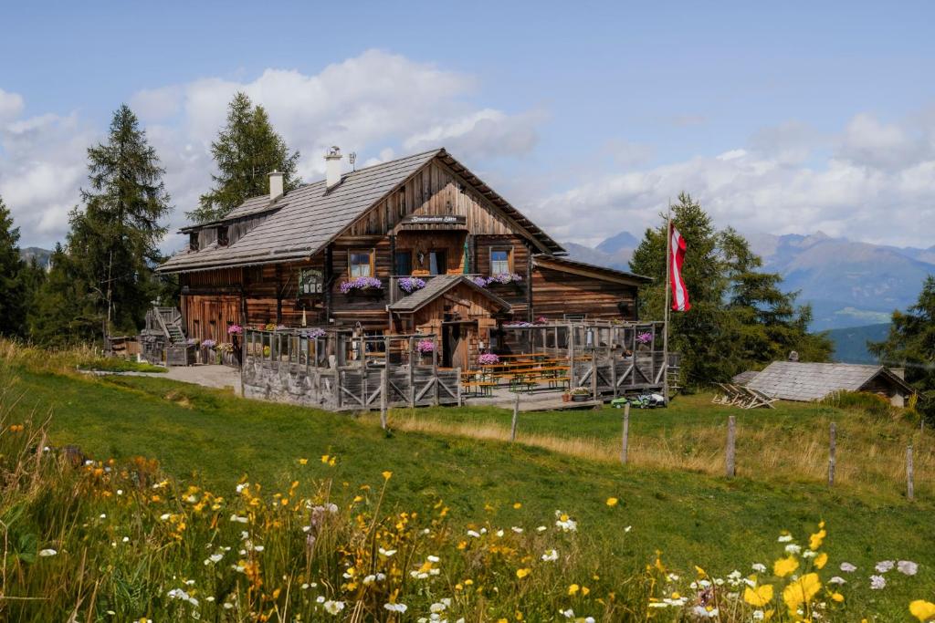 a wooden house on a hill with a field of flowers at Branntweineralm in Tamsweg