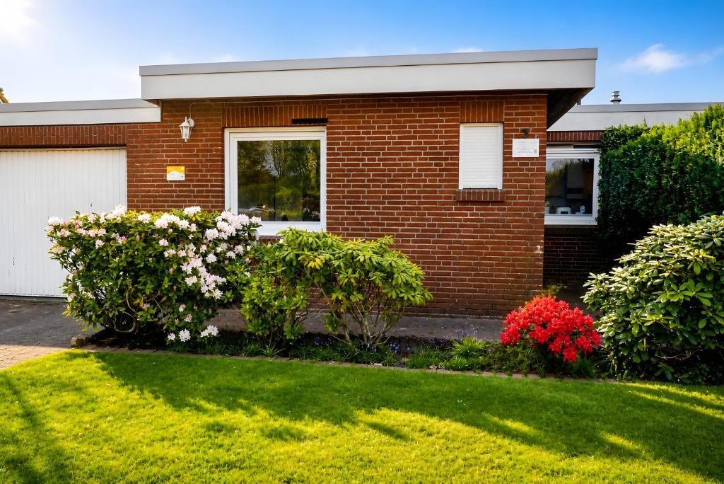 a brick house with a green yard with flowers at Ferienhaus Klaus in Berumbur