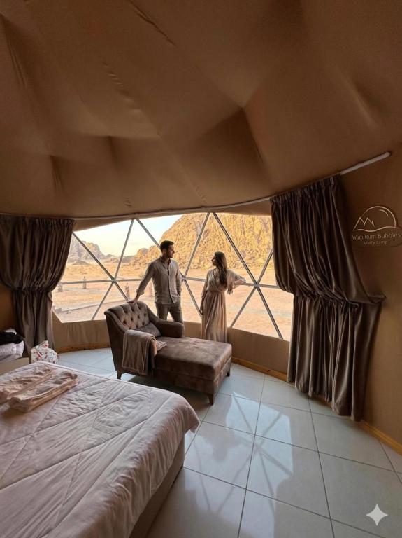 a man and a woman standing in a room with a window at Wadi Rum Bubbles Luxury Camp in Wadi Rum