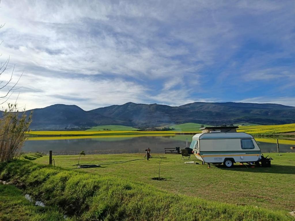 a camper parked in a field next to a lake at Bietjiedam's Campsites in Caledon