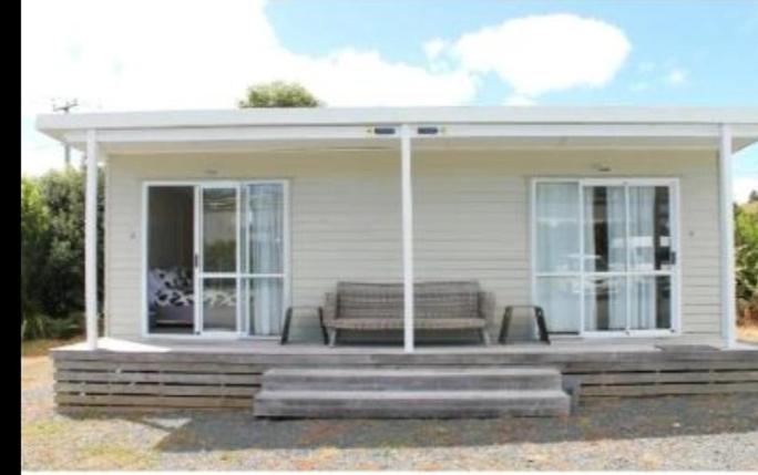 a small white house with a bench on a porch at Raglan park rest and stay cabins - Private studio in Raglan