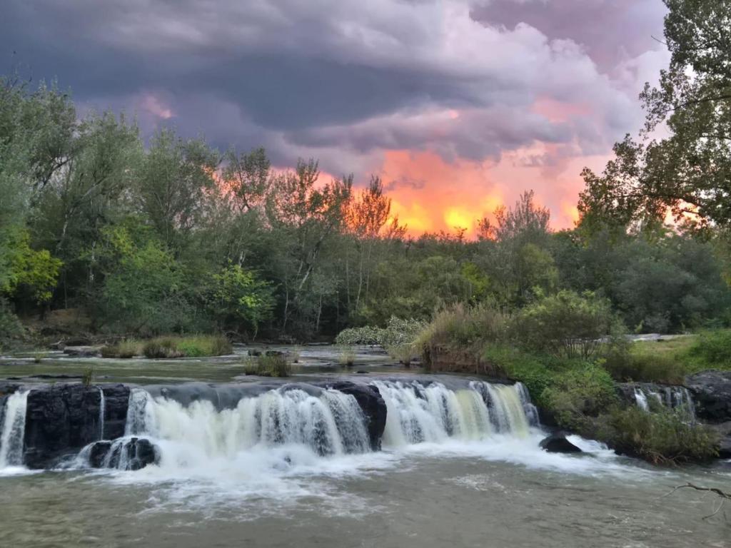 a waterfall in a river with a sunset in the background at River Glen Farm in Winterton