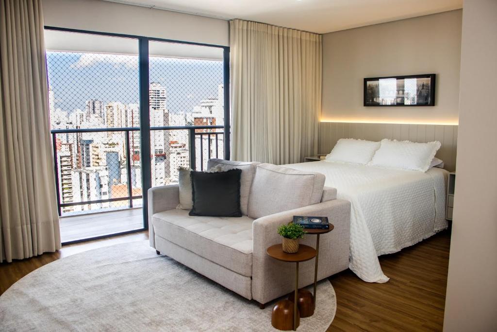 a bedroom with a bed and a couch and a large window at Opus Gyro Vaca Brava Studio Luxo e Aconchego in Goiânia