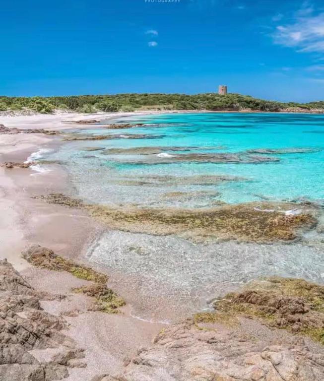a beach with blue water and a lighthouse in the background at Sardegna selvaggia a due passi dal mare in Vignola Mare