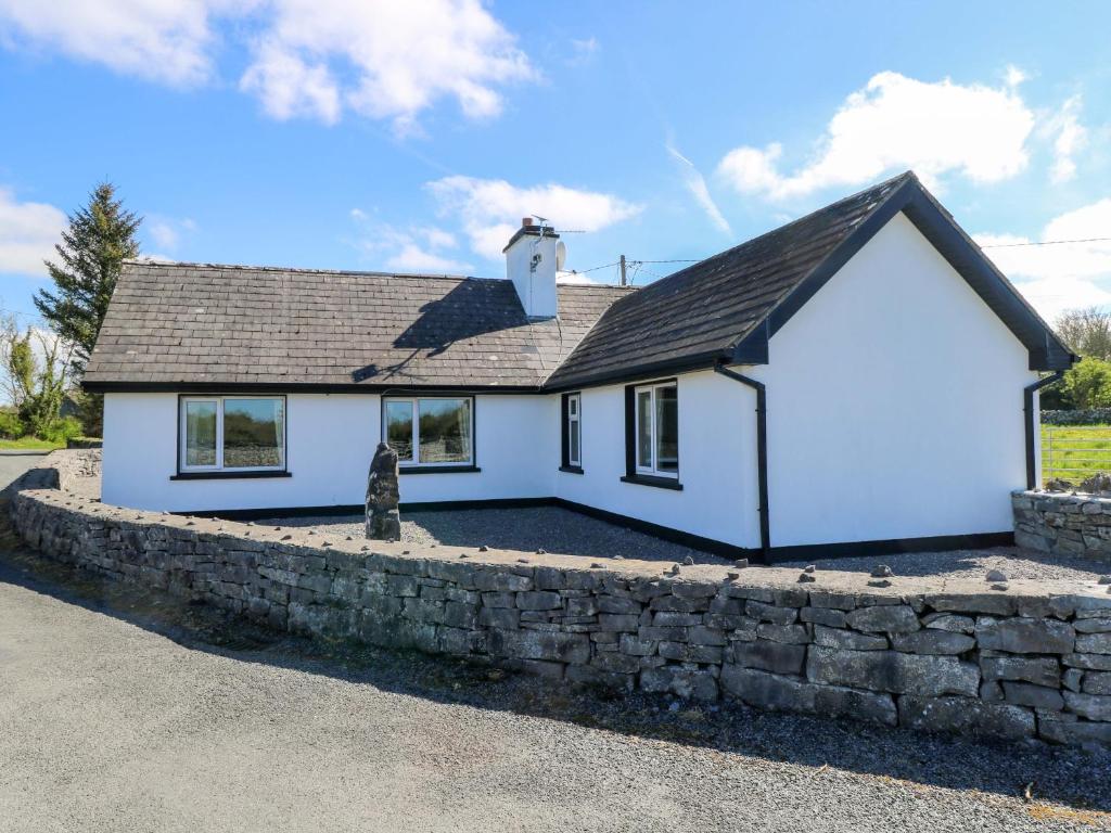 a white house with a stone wall at Cahir Cottage in Ballinrobe