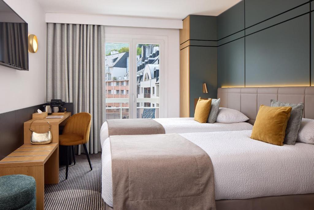 ein Hotelzimmer mit zwei Betten und einem Schreibtisch in der Unterkunft Hôtel Roissy in Lourdes