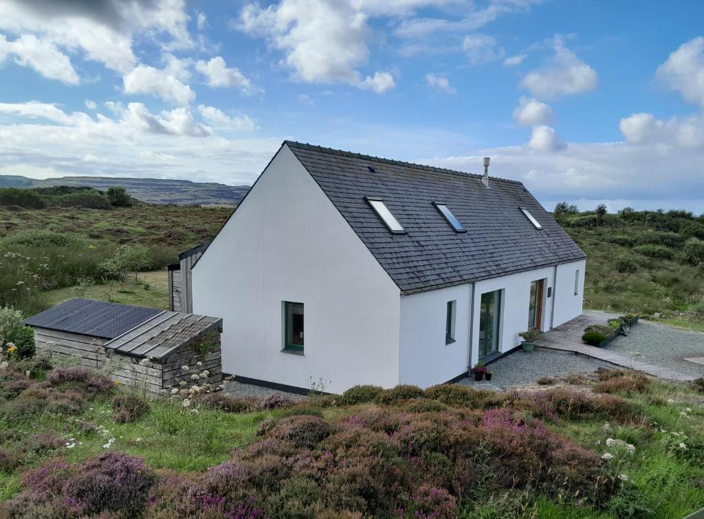 a white house with a black roof on a hill at Modern, eco friendly house in Kildonan on Skye in Flashader