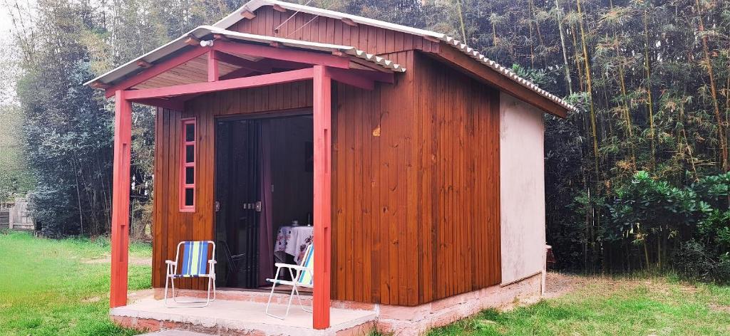 a small wooden shed with two chairs in it at Cabana com Estacionamento ll Internet l Nomade Digital ll Táxi Fácil II Fogão Peq ll Quiosque Churrasqueira ll 5km da ERS-030 Km 88 ll 7Km da Prefeitura l Câmara Mun I IFRGS II 7,2Km UFRGS Litoral II l 12km-Praias in Osório