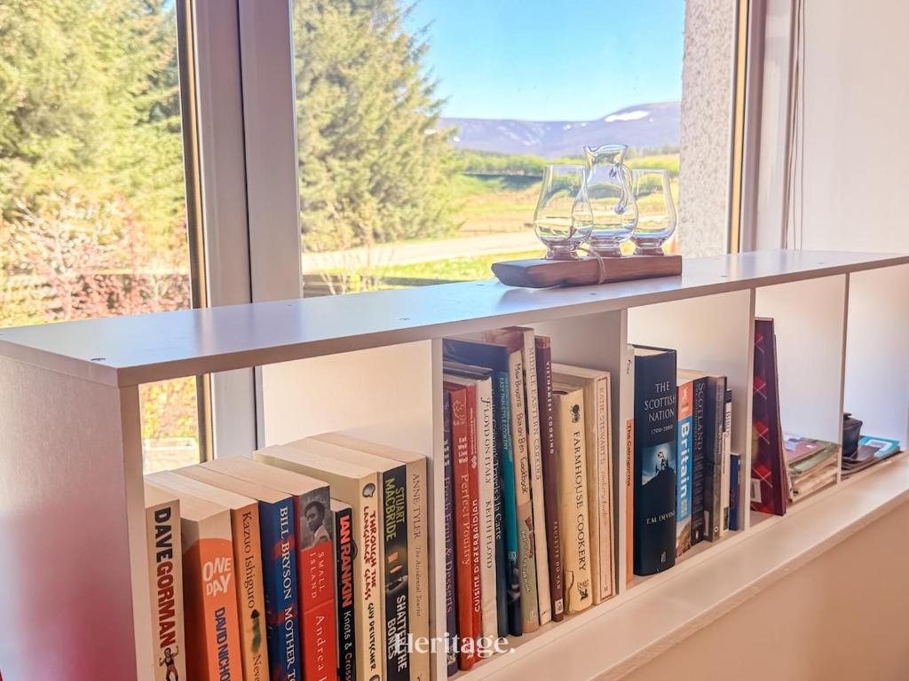 a book shelf filled with books in front of a window at Nether Clashnoir, Glenlivet in Knockandhu