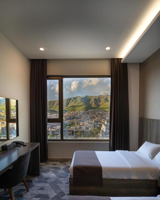 a bedroom with a bed and a desk and a large window at Wan Hotel in Duhok