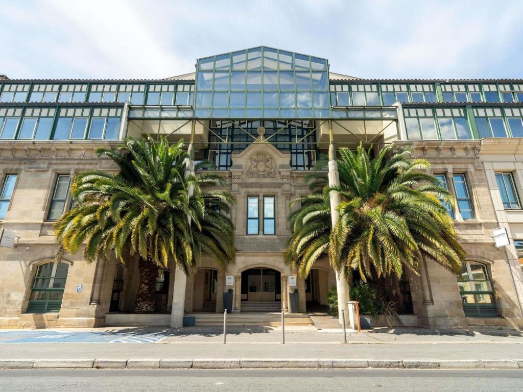 a building with two palm trees in front of it at Mercure Bordeaux Chateau Chartrons in Bordeaux