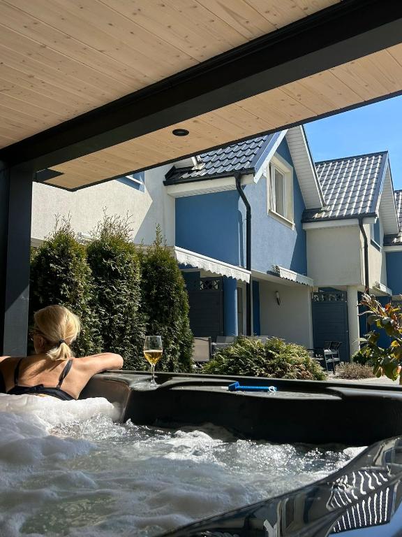 a woman in a hot tub in a backyard with a glass of wine at Domki Kapitańskie Lubiatowo z sauną i balią z jacuzzi in Lubiatowo