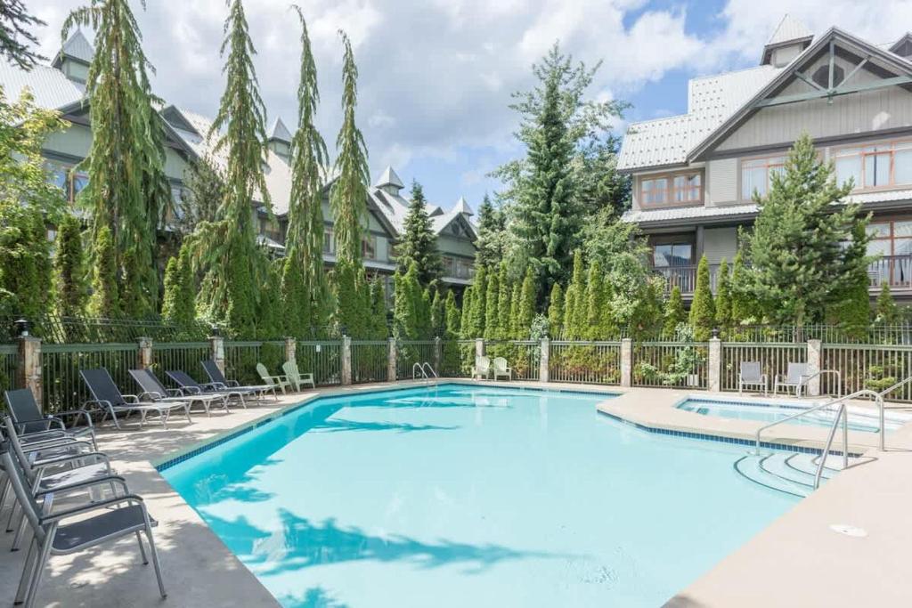 a swimming pool with chairs and a house at Bright and Clean, Walk Everywhere, Shared Pool and Hot Tub in Whistler