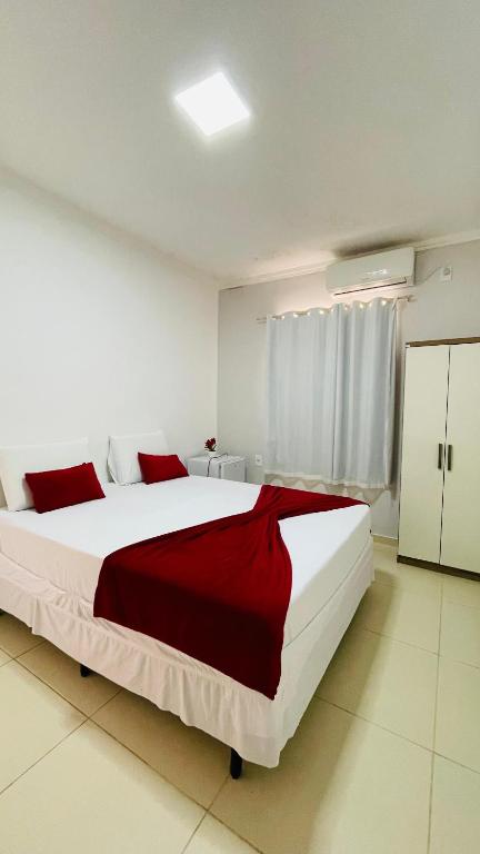 a white bedroom with a large bed with red sheets at Pousada Girassol in Piranhas