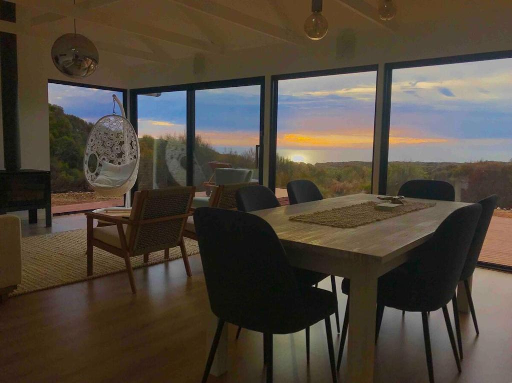 a dining room with a table and chairs and windows at Stokes Bay Cliffs Kangaroo Island in Stokes Bay