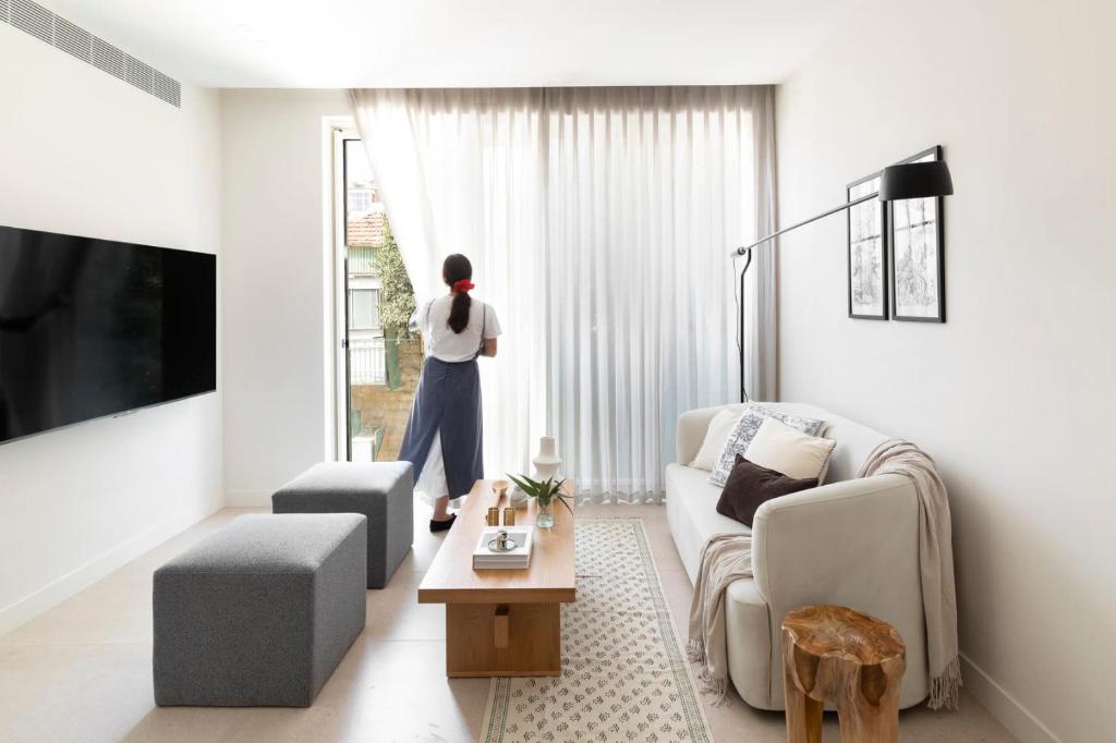 a woman standing in a living room looking out the window at The J Luxury Apartments Near Mahane Yehuda - Perfect for Shabbat Stays in Jerusalem