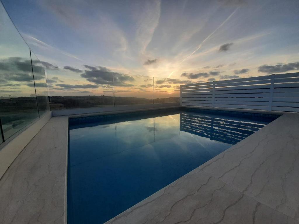 a swimming pool on top of a building with the sunset at Sunsets Duplex Penthouse Gozo in Kerċem