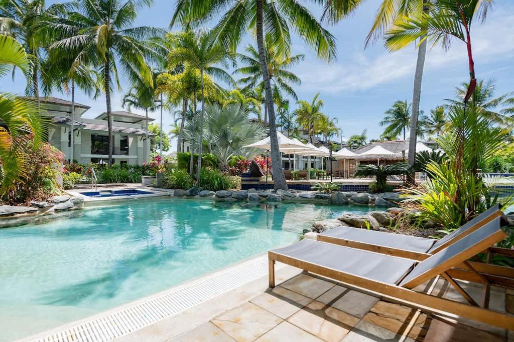 a swimming pool with palm trees and a house at Poolside Relaxation - Resort Retreat with Beach Access in Port Douglas