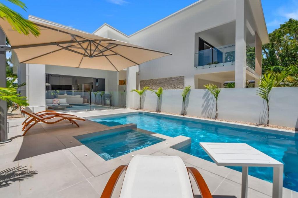 a pool with chairs and an umbrella next to a house at Salt - Beachfront Luxe with Private Pool in Palm Cove