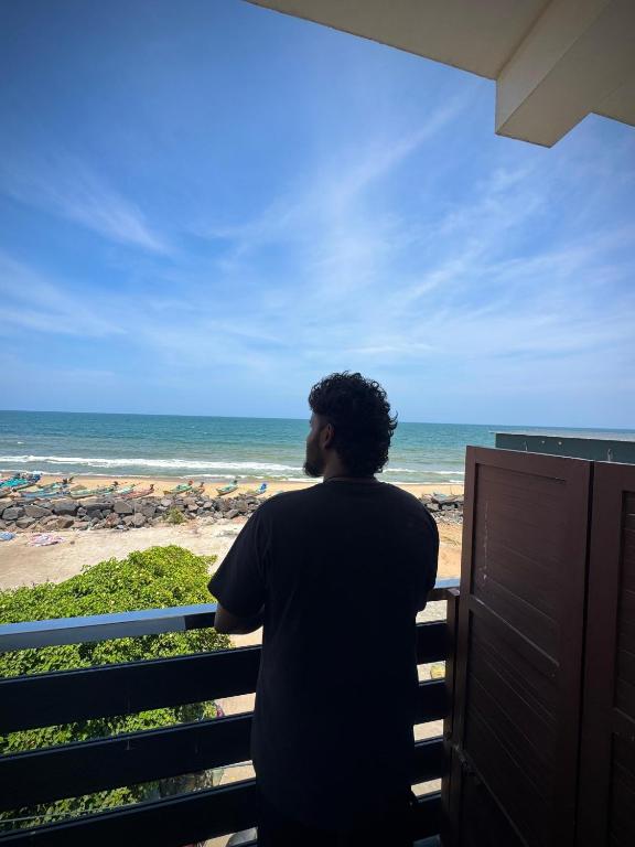 a man standing on a balcony looking out at the ocean at Serenity Beach Inn in Pondicherry
